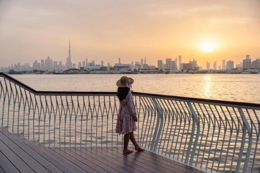 Woman enjoying Dubai skyline by a water body at sunset